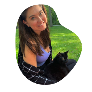 A woman sitting on grass holding her black cat